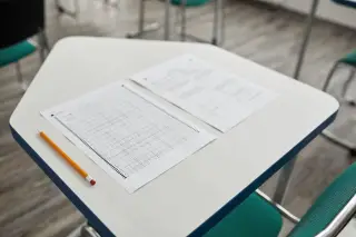 Ilustrasi: Lembar ujian dan sebuah pensil diletakkan di atas meja kelas yang bersih.