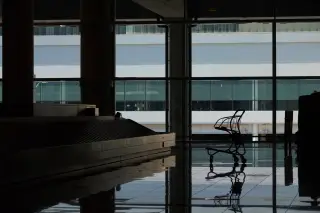 Ilustrasi: Siluet troli barang dan ban berjalan bagasi di dekat jendela kaca besar terminal bandara.