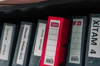 Ilustrasi: Deretan map binder arsip tersusun di rak dengan satu binder berwarna merah mencolok.