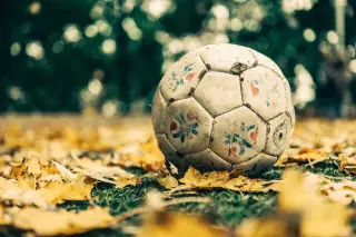 Ilustrasi: Sebuah bola sepak usang tergeletak di atas rumput berdaun gugur.