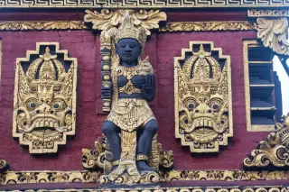 Ilustrasi: Detail ukiran patung dan ornamen berwarna emas pada dinding bangunan pura di Bali.