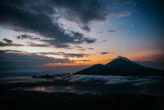 Ilustrasi: Pemandangan siluet gunung dan danau berselimut awan saat matahari terbit.