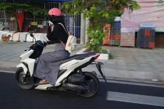 Ilustrasi: Seorang pengendara motor berhelm merah muda melintas di jalan raya.