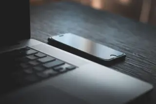 Ilustrasi: Sebuah laptop dan ponsel pintar diletakkan di atas meja kayu berwarna gelap.