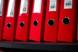 Ilustrasi: Deretan map binder merah tersusun rapi di rak kantor.