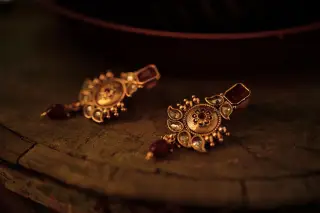 Ilustrasi: Sepasang anting emas berukir dengan batu permata tergeletak di atas permukaan kayu.