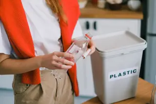 Ilustrasi: Seseorang memegang botol plastik di samping tempat sampah berlabel plastik di dalam dapur.