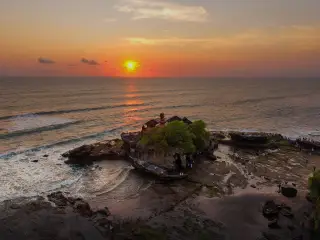 Ilustrasi: Pemandangan udara Pura Tanah Lot di tepi laut dengan latar matahari terbenam.