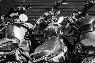Ilustrasi: Deretan stang dan tangki sepeda motor yang terparkir rapat dalam foto hitam putih.