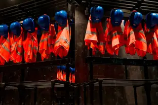 Ilustrasi: Deretan rompi oranye dan helm proyek biru tergantung rapi di loker besi.