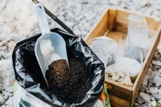 Ilustrasi: Sekop plastik di dalam kantong berisi tanah subur di samping kotak kayu.