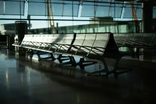 Ilustrasi: Deretan kursi tunggu bandara yang kosong di dekat dinding kaca besar.