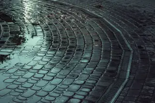 Ilustrasi: Genangan air di atas jalan paving melingkar basah dengan saluran drainase kecil.