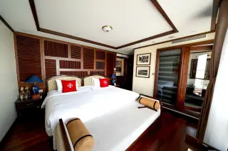 Ilustrasi: Interior kamar hotel mewah dengan tempat tidur ganda bernuansa kayu dan bantal merah.