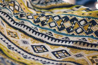 Ilustrasi: Foto jarak dekat sehelai kain tenun bermotif geometris dengan dominasi warna kuning dan biru.
