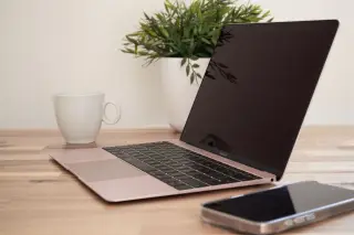 Ilustrasi: Laptop terbuka, ponsel, cangkir putih, dan tanaman pot di atas meja kayu.
