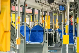 Ilustrasi: Interior bus umum dengan deretan kursi biru dan tiang pegangan kuning.