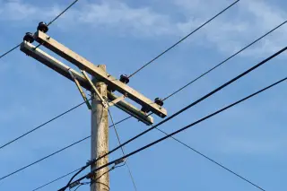 Ilustrasi: Tiang listrik kayu dengan kabel-kabel membentang berlatar belakang langit biru.