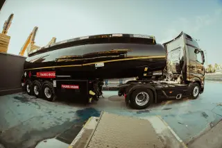 Ilustrasi: Truk tangki bahan bakar hitam terparkir di area industri dengan lensa sudut lebar.