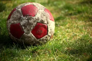 Ilustrasi: Sebuah bola sepak usang berwarna merah putih tergeletak di atas rumput hijau.