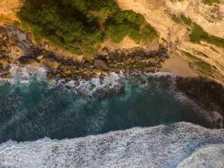 Ilustrasi: Pemandangan udara tebing pantai berbatu dengan deburan ombak berbusa putih.