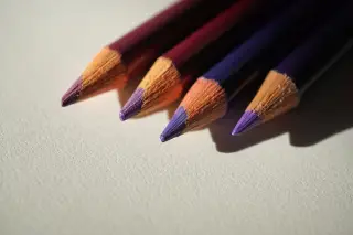 Ilustrasi: Empat buah pensil warna bernuansa ungu di atas kertas putih bertekstur.