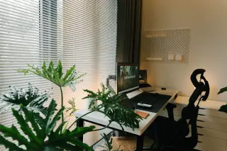 Ilustrasi: Ruang kerja rapi dengan meja, monitor komputer, kursi kerja, dan tanaman hias di dekat jendela.