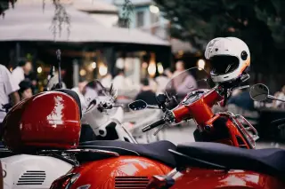 Ilustrasi: Helm putih terpasang di atas stang skuter merah yang sedang terparkir.