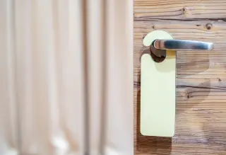 Ilustrasi: Gantungan pintu polos tergantung pada gagang pintu kayu sebuah kamar hotel.
