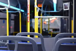 Ilustrasi: Bagian dalam bus kota yang kosong dengan kursi dan tiang pegangan tangan kuning.
