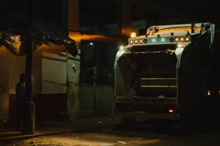 Ilustrasi: Bagian belakang truk sampah yang terparkir di tepi jalan pada malam hari.