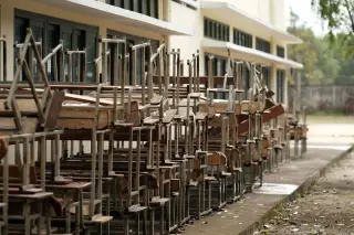 Ilustrasi: Tumpukan meja dan kursi sekolah tua tersusun di luar gedung sekolah.