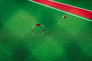Ilustrasi: Gawang kecil gateball bernomor satu dan bola di atas lapangan rumput sintetis hijau.