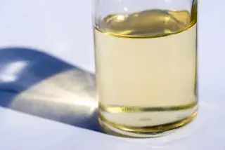 Ilustrasi: Sebuah botol kaca berisi cairan kekuningan di atas permukaan putih dengan bayangan.
