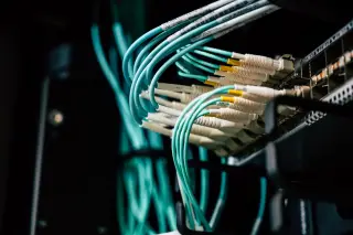 Ilustrasi: Deretan kabel jaringan serat optik terhubung ke panel server data center.