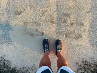 Ilustrasi: Sepasang kaki bersepatu lari berdiri di atas pasir dengan jejak sepatu lainnya di depannya.