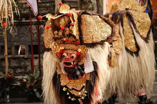 Ilustrasi: Kostum Barong tradisional Bali dengan hiasan emas dan bulu putih di area pura.