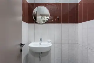 Ilustrasi: Wastafel putih dengan cermin bundar di toilet berdinding keramik.