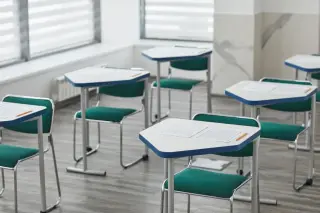Ilustrasi: Deretan meja dan kursi kosong di dalam sebuah ruang kelas modern dengan kertas ujian di atasnya.