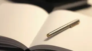 Ilustrasi: Buku catatan terbuka dengan pena logam terletak di atas halaman kosong.
