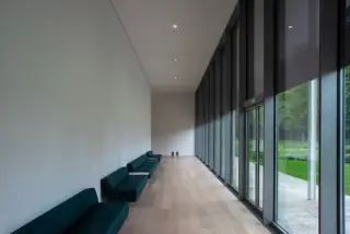Ilustrasi: Lorong gedung modern yang sepi dengan deretan sofa hijau dan dinding kaca besar.