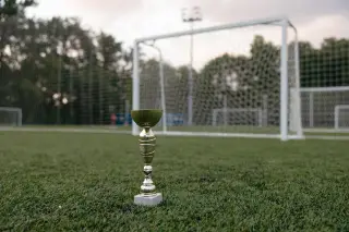 Ilustrasi: Sebuah piala berdiri di atas rumput lapangan sepak bola dengan latar belakang gawang.