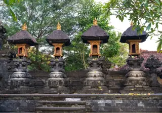 Ilustrasi: Deretan pelinggih pura khas Bali beratap ijuk dengan latar pepohonan hijau.
