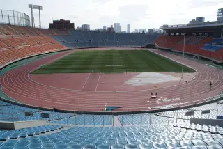 Ilustrasi: Pemandangan stadion sepak bola dan lintasan atletik yang luas dengan tribun kursi kosong.