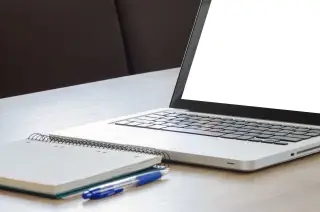 Ilustrasi: Sebuah laptop terbuka dengan layar putih kosong, buku catatan spiral, dan pulpen di atas meja.