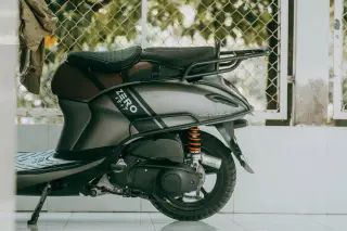 Ilustrasi: Bagian belakang sepeda motor matik abu-abu yang terparkir di dekat pagar kawat.