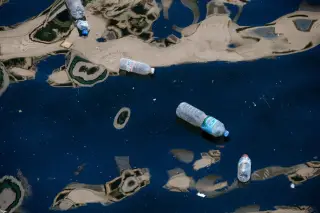 Ilustrasi: Beberapa botol plastik bekas mengapung di permukaan air yang gelap dan bergelombang.