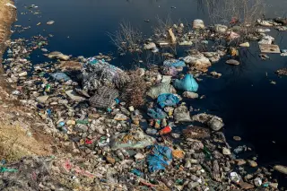 Ilustrasi: Tumpukan sampah plastik dan limbah mengotori tepi perairan yang gelap.