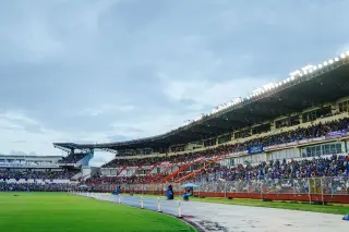 Ilustrasi: Tribun stadion olahraga dipadati penonton di samping lapangan hijau dan lintasan lari.