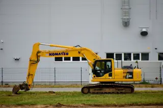 Ilustrasi: Satu unit ekskavator berwarna kuning terparkir di dekat dinding bangunan abu-abu.